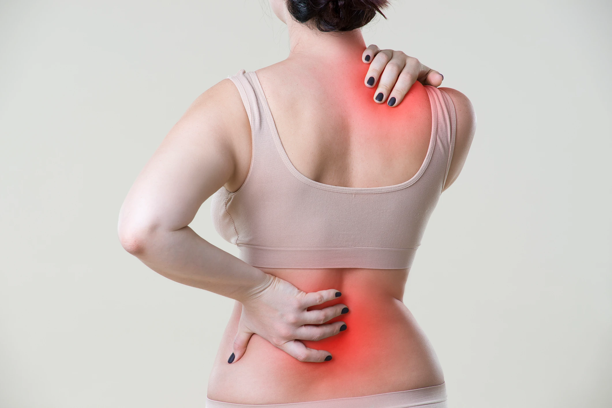 A woman seen from behind holds her lower back and shoulder, with both areas highlighted in red