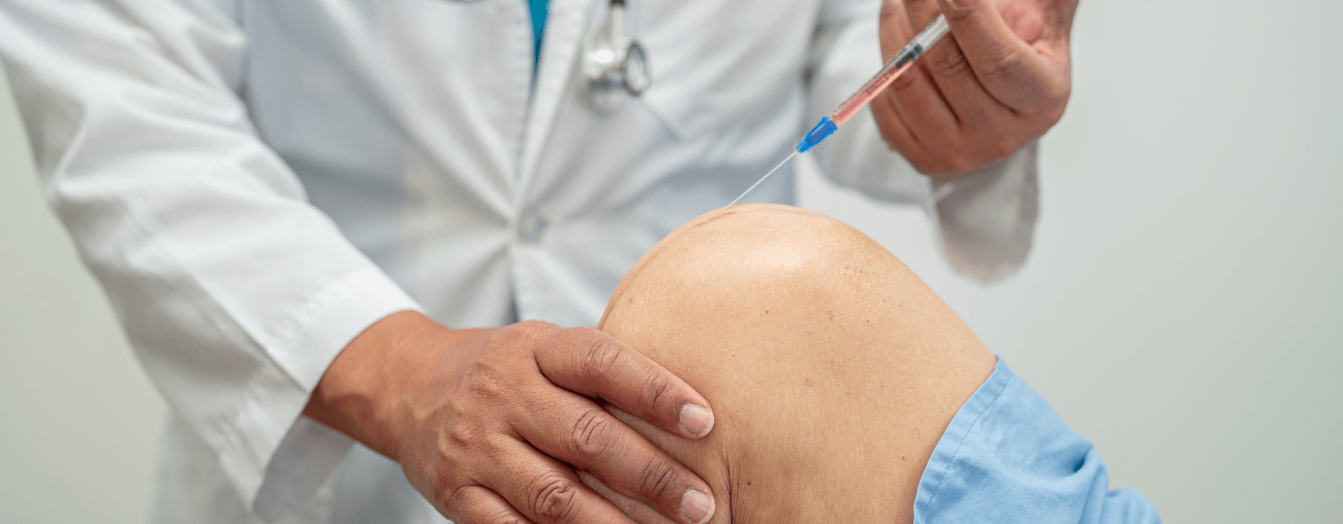 A physician in a white coat steadies a patient’s knee with one hand and holds a syringe in the other