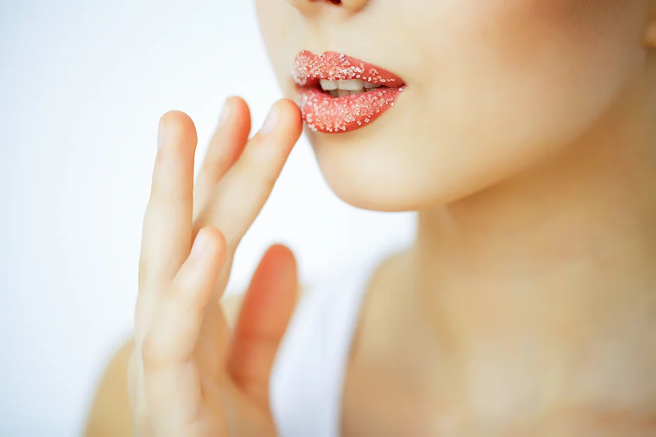 a woman uses lip scrub to exfoliate her lips