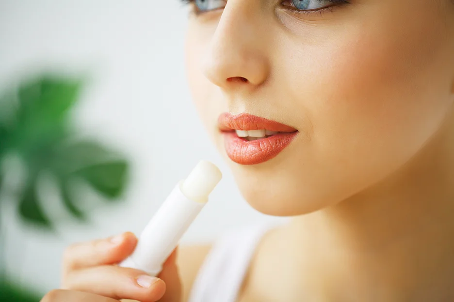 a woman applies lip balm on her plump lips