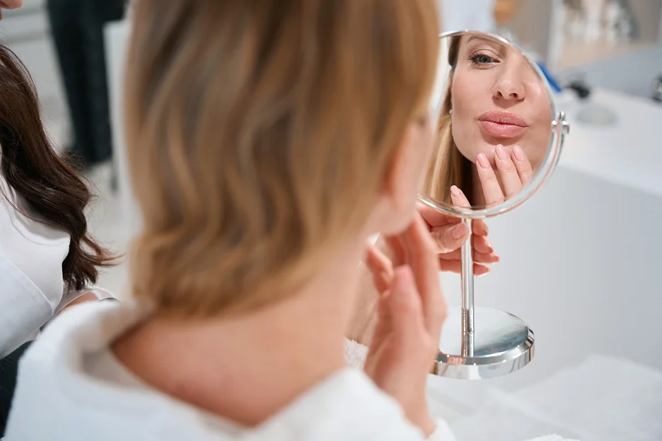 a woman checks her lips in front of the mirror during lip filler consultation inside a med spa