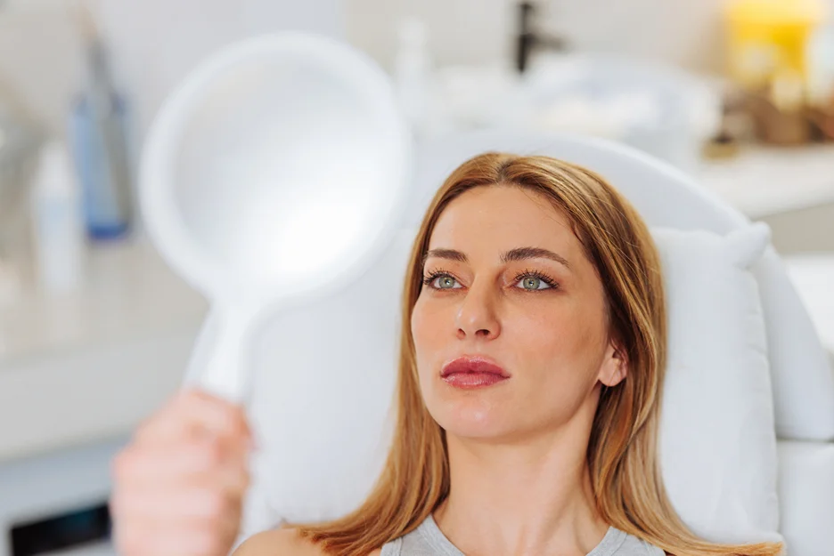 a woman checks her lips in front of the mirror after lip filler procedure